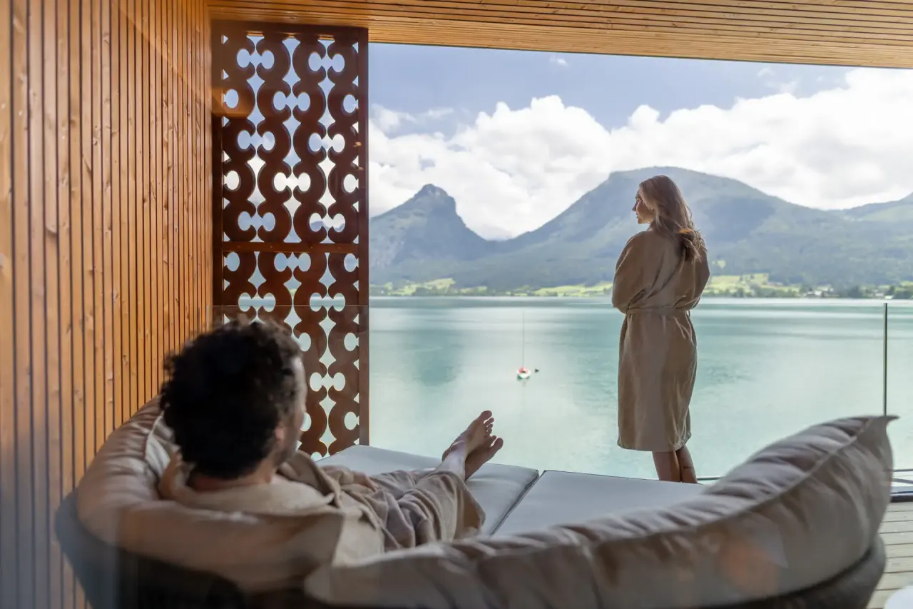 Gäste entspannen im Bademantel mit Seeblick und Bergpanorama im Wellnessbereich des Hotel Seevilla Wolfgangsee.