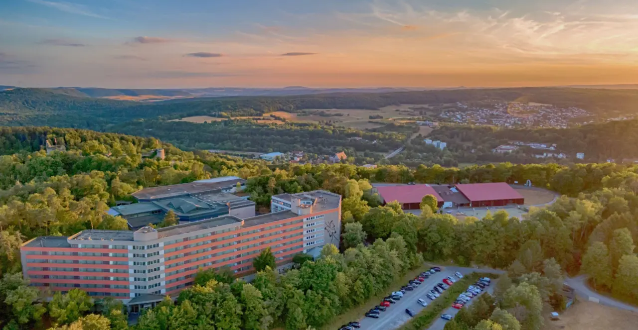 Luftaufnahme des Hotel Sonnenhügel Familotel Rhön bei Sonnenuntergang, eingebettet in die grüne Landschaft der Rhön.