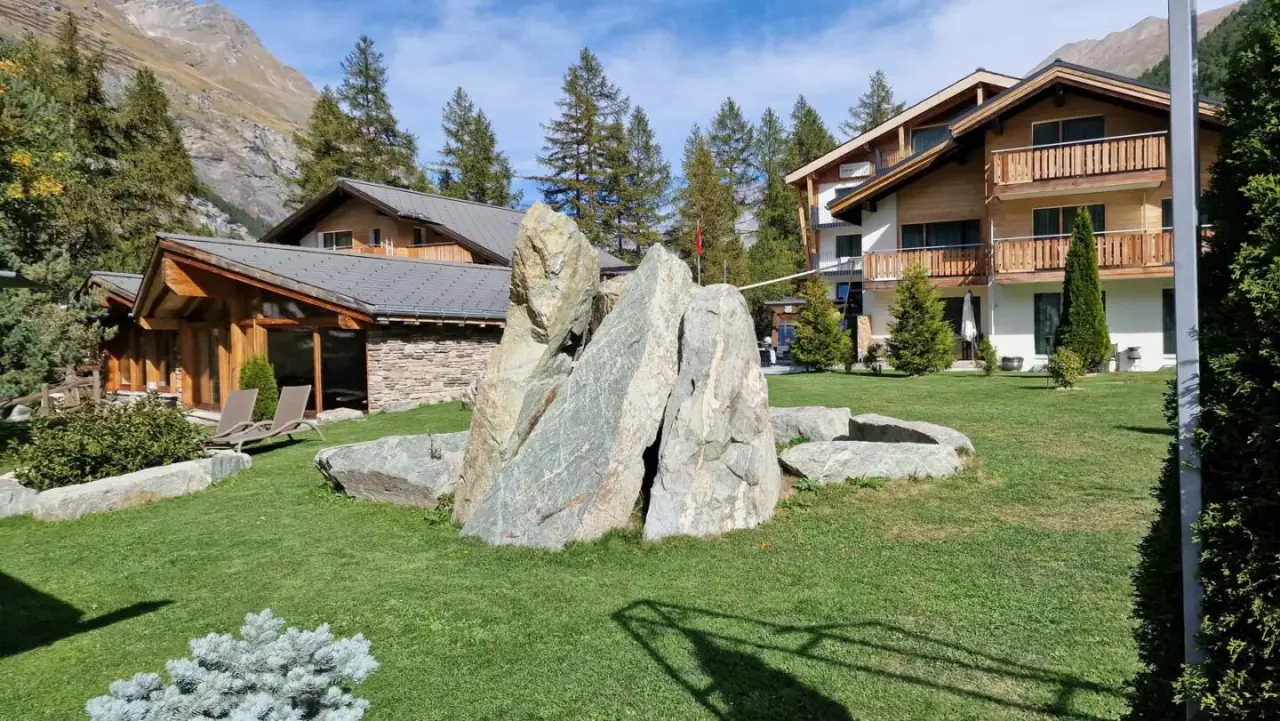 Aussenansicht des Hotel Hemizeus und Iremia Spa mit alpiner Landschaft, Holzfassaden, Garten und grossen Felsen.
