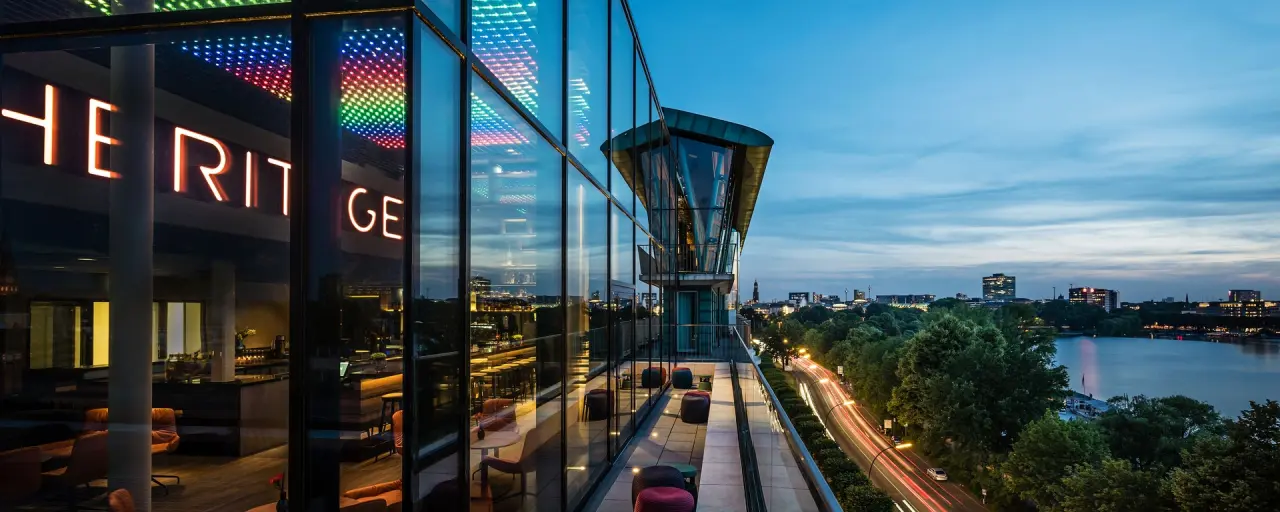 Abendansicht des Royal Meridien Hamburg mit moderner Glasfassade, beleuchteter Bar und Panoramablick über die Alster.