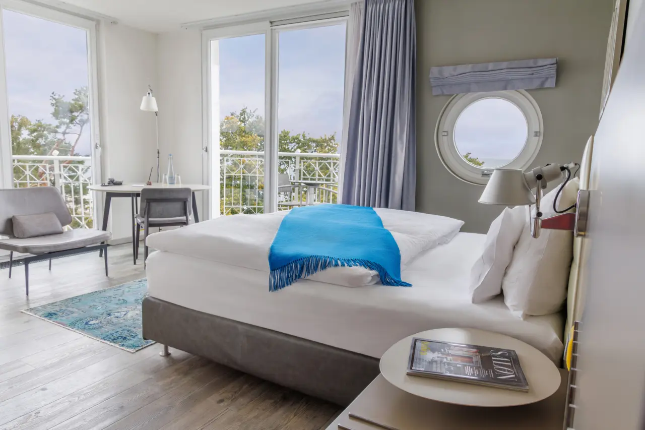 Helles Hotelzimmer im Hotel Am Meer & Spa mit Doppelbett, Meerblick und Balkon. Modernes Design mit Bullaugenfenster.