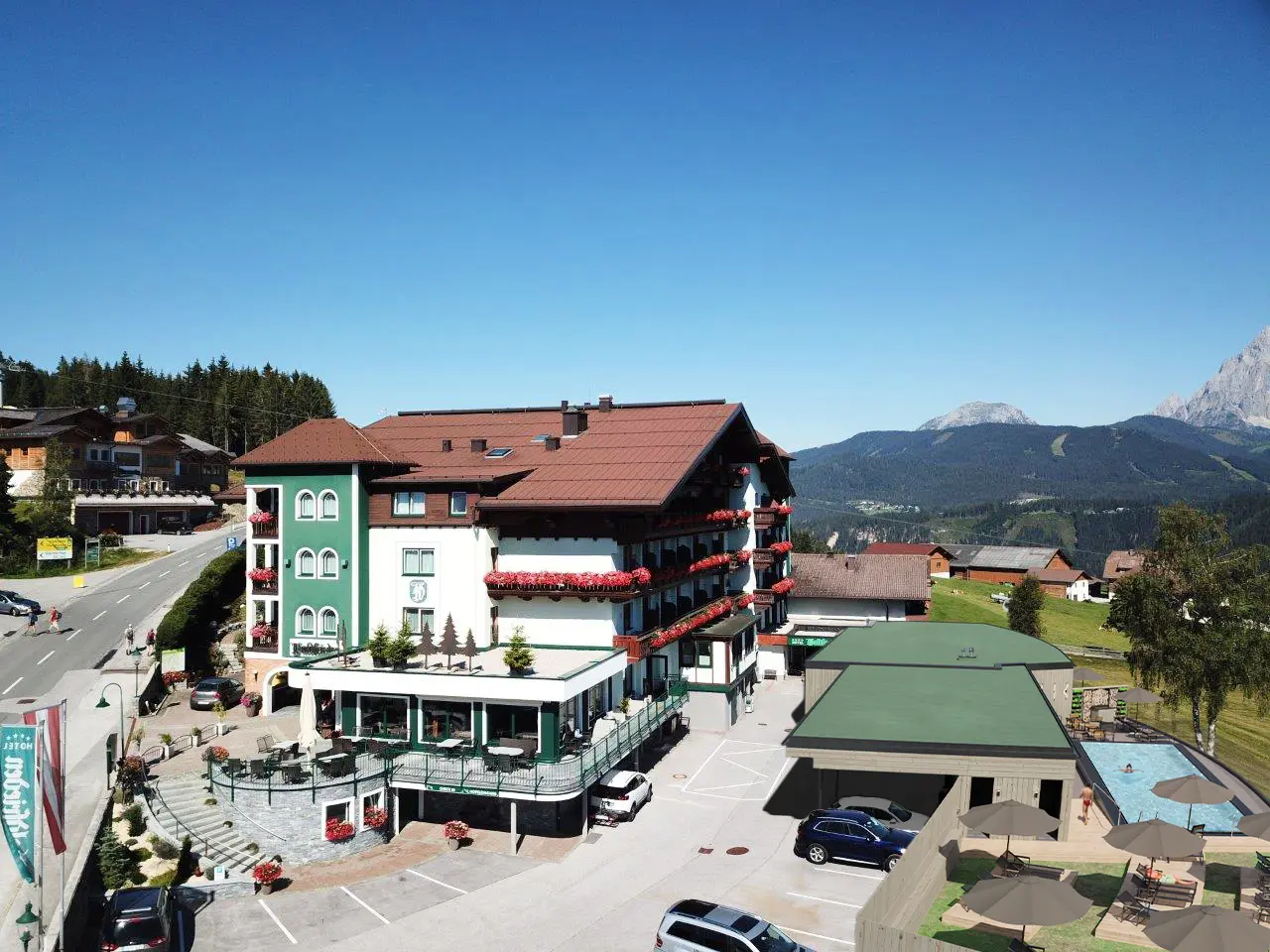 Luftaufnahme des Hotel Waldfrieden mit traditioneller Architektur, blumengeschmückten Balkonen, Aussenpool und Bergpanorama.