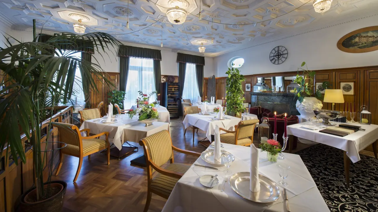 Elegantes Restaurant mit festlich gedeckten Tischen und Stuckdecke im Wellnesshotel Palmenwald.