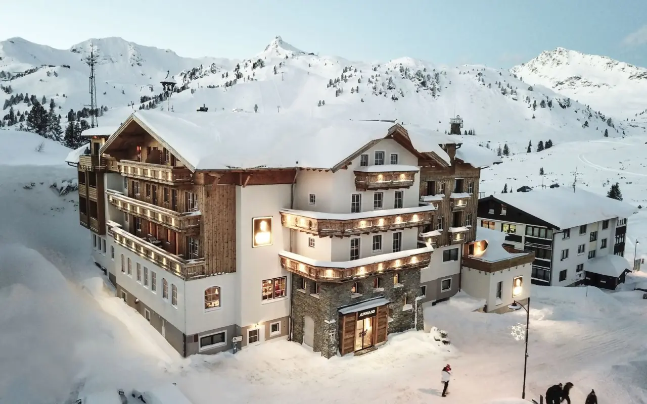Das Hotel Alpenland im Winter, eingebettet in eine verschneite Berglandschaft. Die beleuchtete Fassade strahlt Wärme und Gemütlichkeit aus.