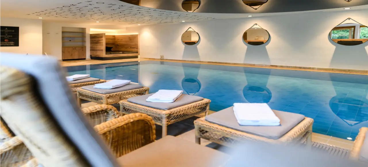 Einladender Innenpool mit bequemen Rattan-Liegen und Entspannungsbereich im Wellnesshotel Staudacherhof.
