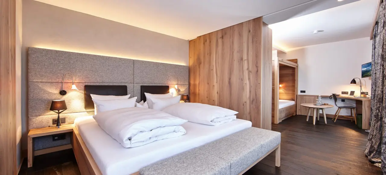 Geräumiges Hotelzimmer im Staudacherhof mit Doppelbett, Holzelementen und separatem Schlafbereich.