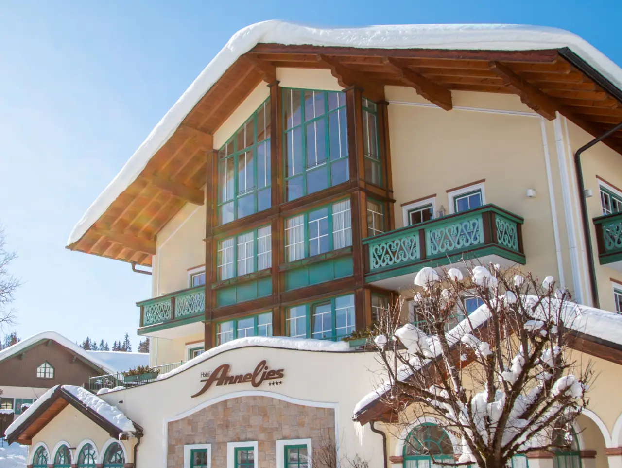 Hotel Annelies in winter mit verschneitem Dach und traditioneller alpiner Architektur unter blauem Himmel.