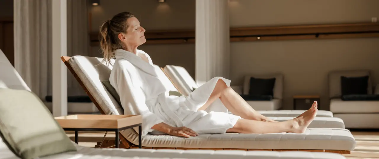 Entspannte Frau im Bademantel auf einer Liege im Ruheraum des Spa-Bereichs im Hotel Annelies, mit warmem Sonnenlicht.