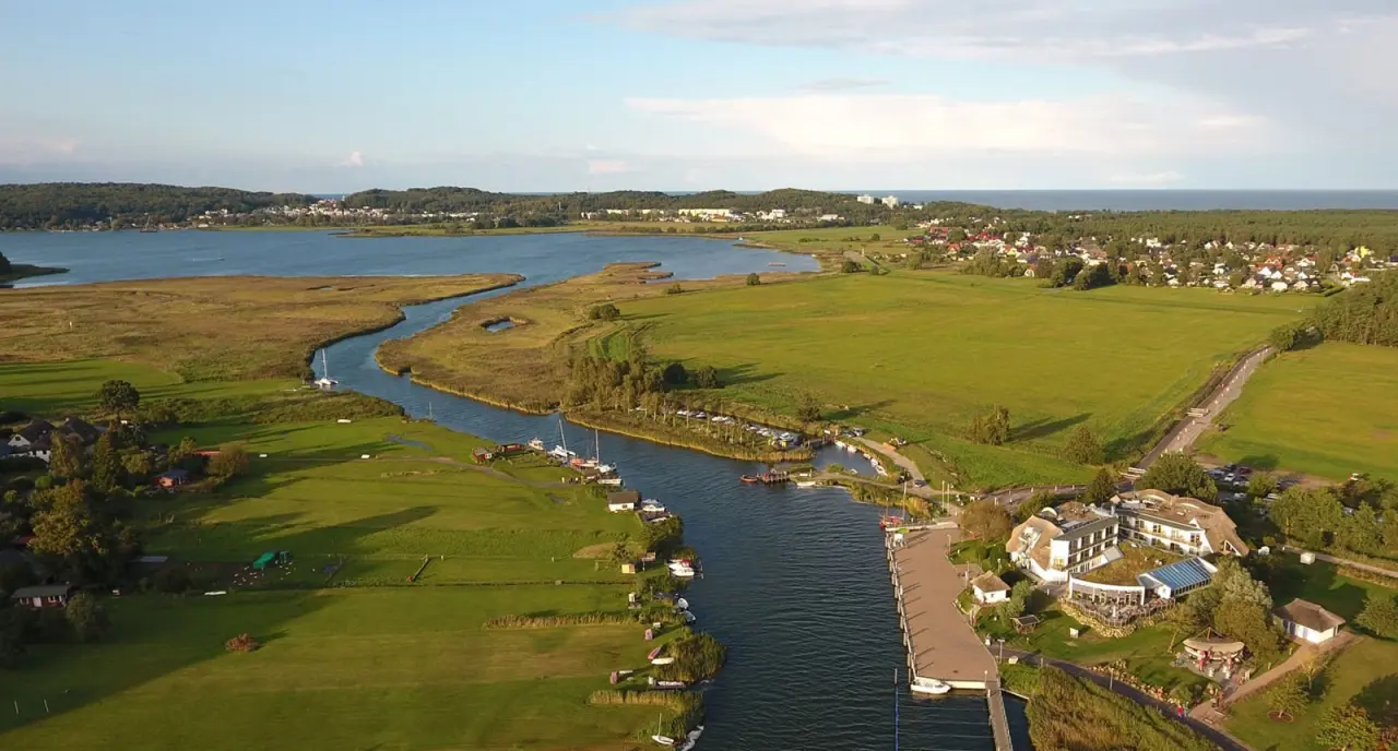 Luftaufnahme vom Hotel Solthus am See mit malerischer Flusslandschaft, grünen Wiesen und dem Bodden im Hintergrund.