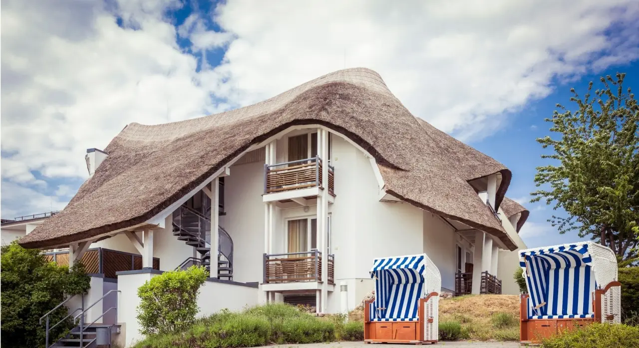 Reetgedecktes Hotel Solthus am See mit blauen Strandkörben unter blauem Himmel, einladende Aussenansicht.