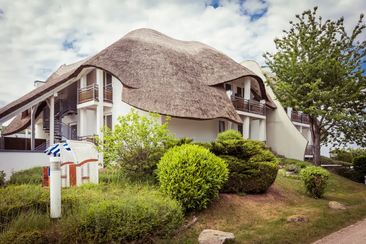 Charmantes Reetdachhotel Solthus am See mit Strandkorb und grüner Gartenanlage unter blauem Himmel.