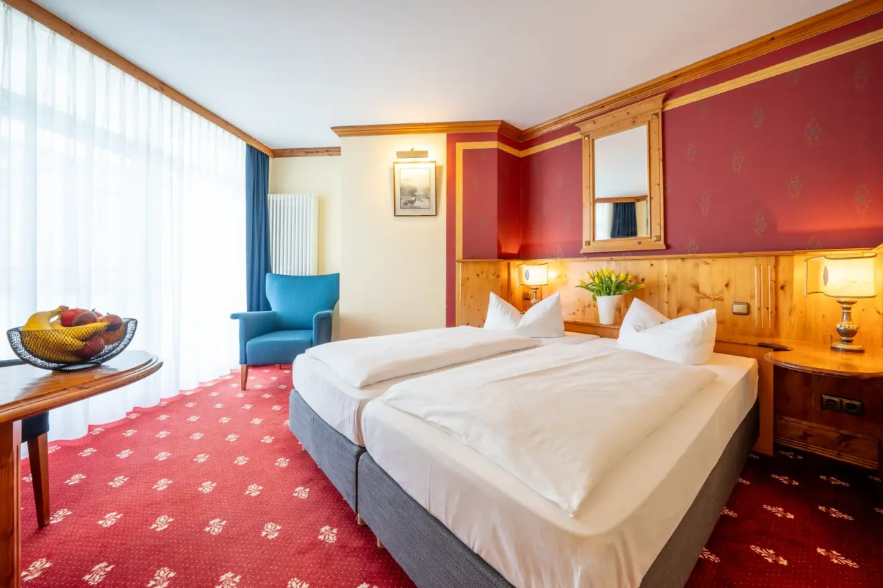 Gemütliches Doppelzimmer im Hotel Solthus am See mit rotem Teppich, Holzvertäfelung und frischem Obst.
