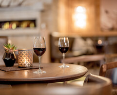 Zwei Gläser Rotwein auf einem Holztisch mit Kerzenlicht in der gemütlichen Lounge des Hotel Regina.