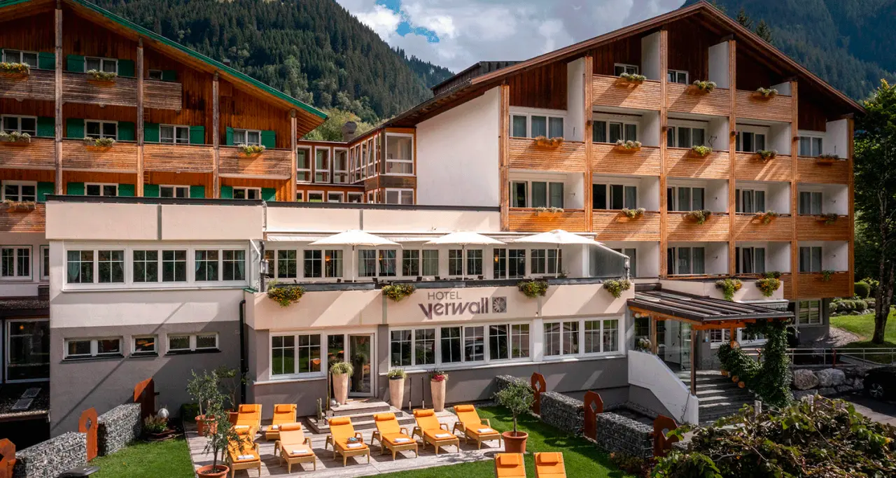Aussenansicht des Hotel Verwall mit alpiner Architektur, Holzfassaden, Balkonen und Sonnenterrasse mit Liegestühlen vor Bergkulisse.