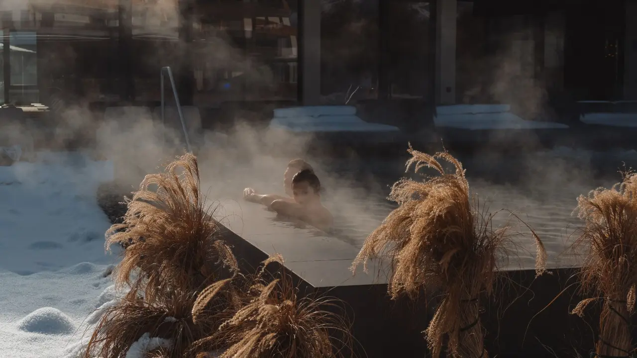 Winter-Wellness im Sport- und Wellnesshotel Held****s: Gäste entspannen im dampfenden Aussenpool umgeben von Schnee.