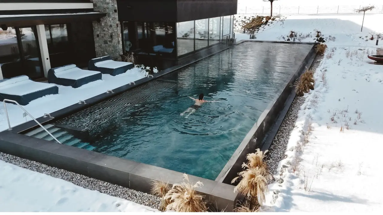 Beheizter Aussenpool im Schnee des Sport- und Wellnesshotel Held****s. Ein Gast schwimmt im warmen Wasser umgeben von Winterlandschaft.