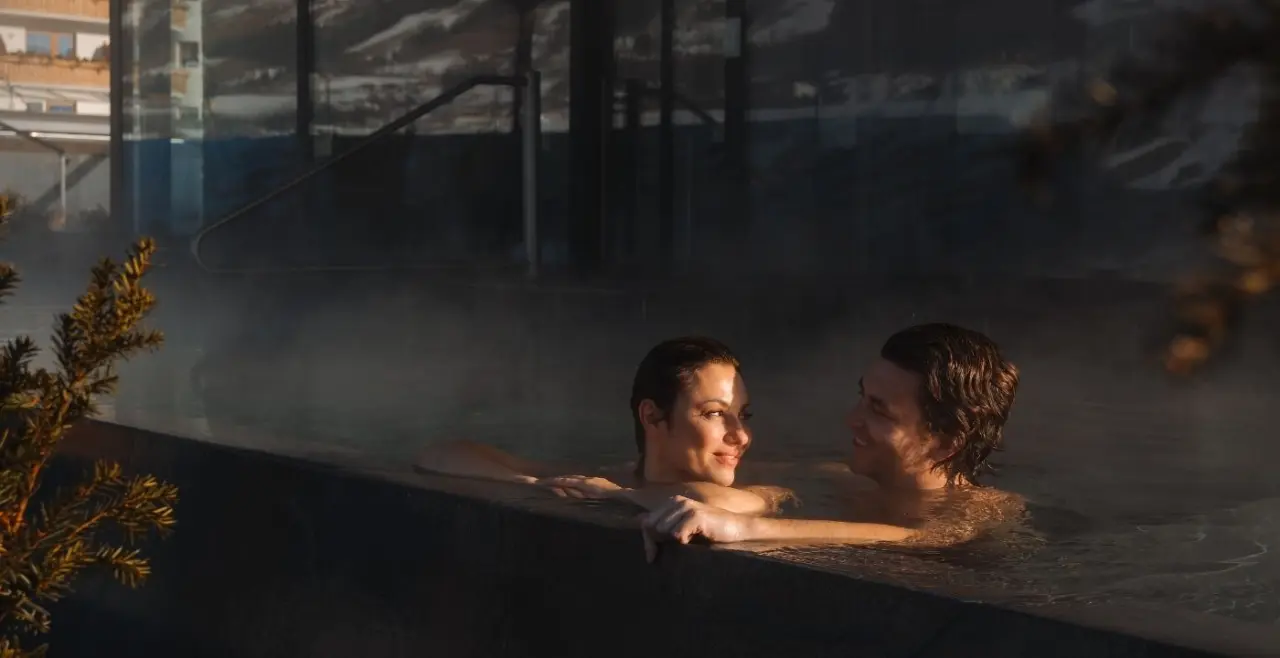 Paar entspannt im dampfenden Aussenpool des Sport- und Wellnesshotel Held****s bei Sonnenuntergang.