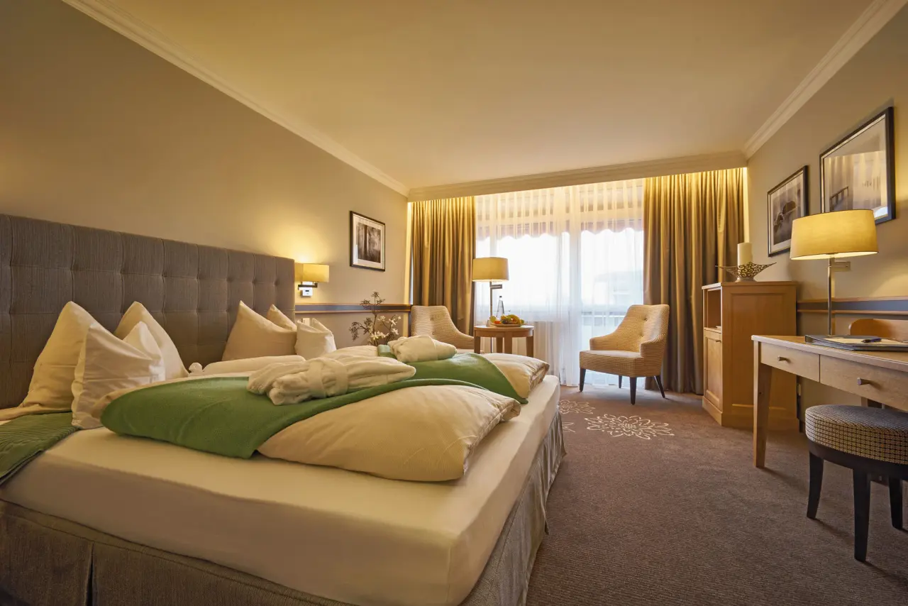 Gemütliches Doppelzimmer im Hotel Apollo mit bequemen Betten, Sitzbereich, Schreibtisch und Bademänteln für Entspannung.