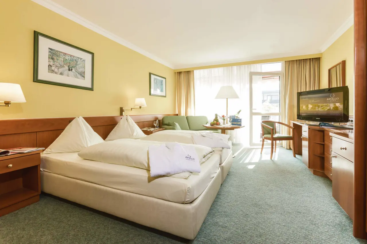 Helles Doppelzimmer im Hotel Apollo mit Balkon, bequemen Betten und Bademänteln für einen entspannten Aufenthalt.