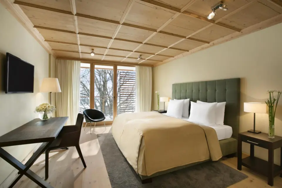 Komfortables Doppelzimmer im Kempinski Hotel Das Tirol mit Holzbalkendecke, Schreibtisch und Balkonblick.
