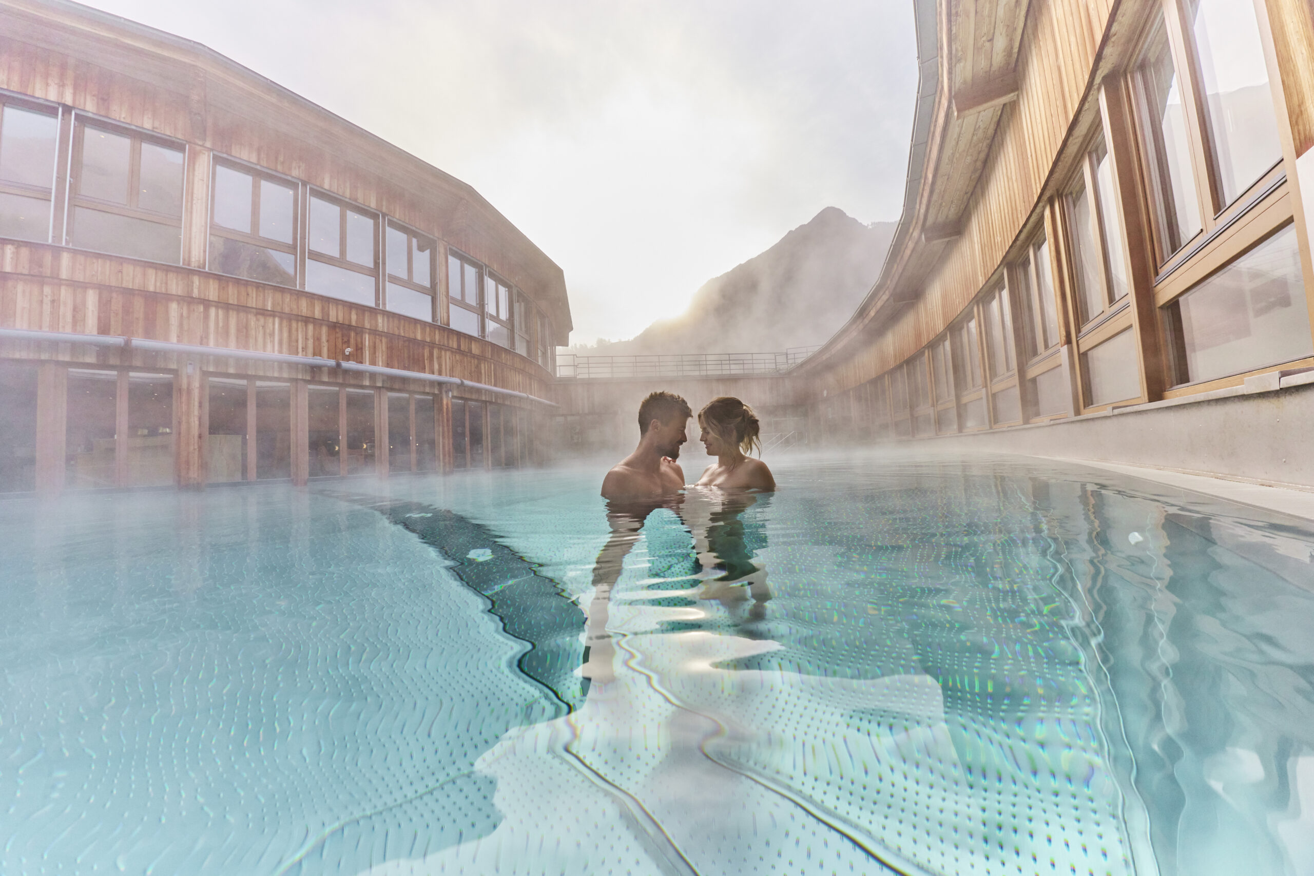 AQUA DOME - Tirol Therme Längenfeld in Längenfeld – Paar entspannt im dampfenden Außenpool | Wellnesshotel Tirol