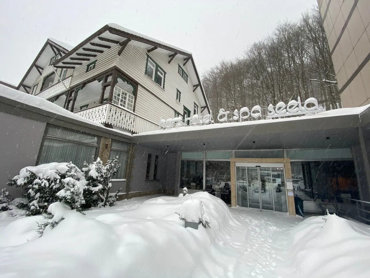 Verschneiter Hoteleingang des Hotel & Spa Seela im Winter mit traditioneller Fassade und tiefem Schnee.