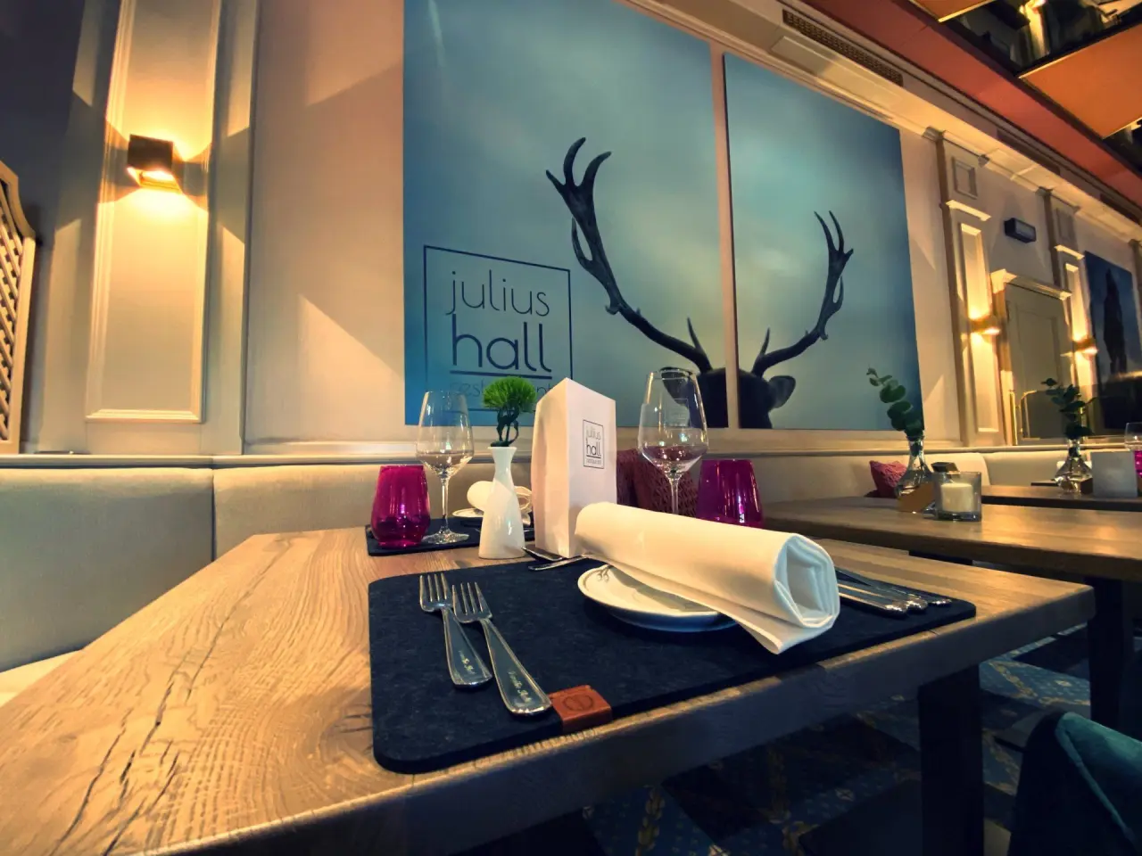 Elegant gedeckter Tisch im Restaurant Julius Hall des Hotel Seela mit Hirschmotiv an der Wand.