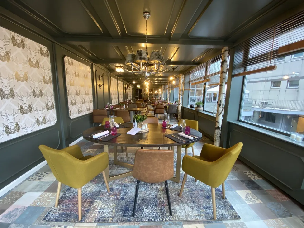 Gemütliches Restaurant im Hotel Seela mit elegant gedeckten Tischen, Hirsch-Tapete und Blick nach draußen.