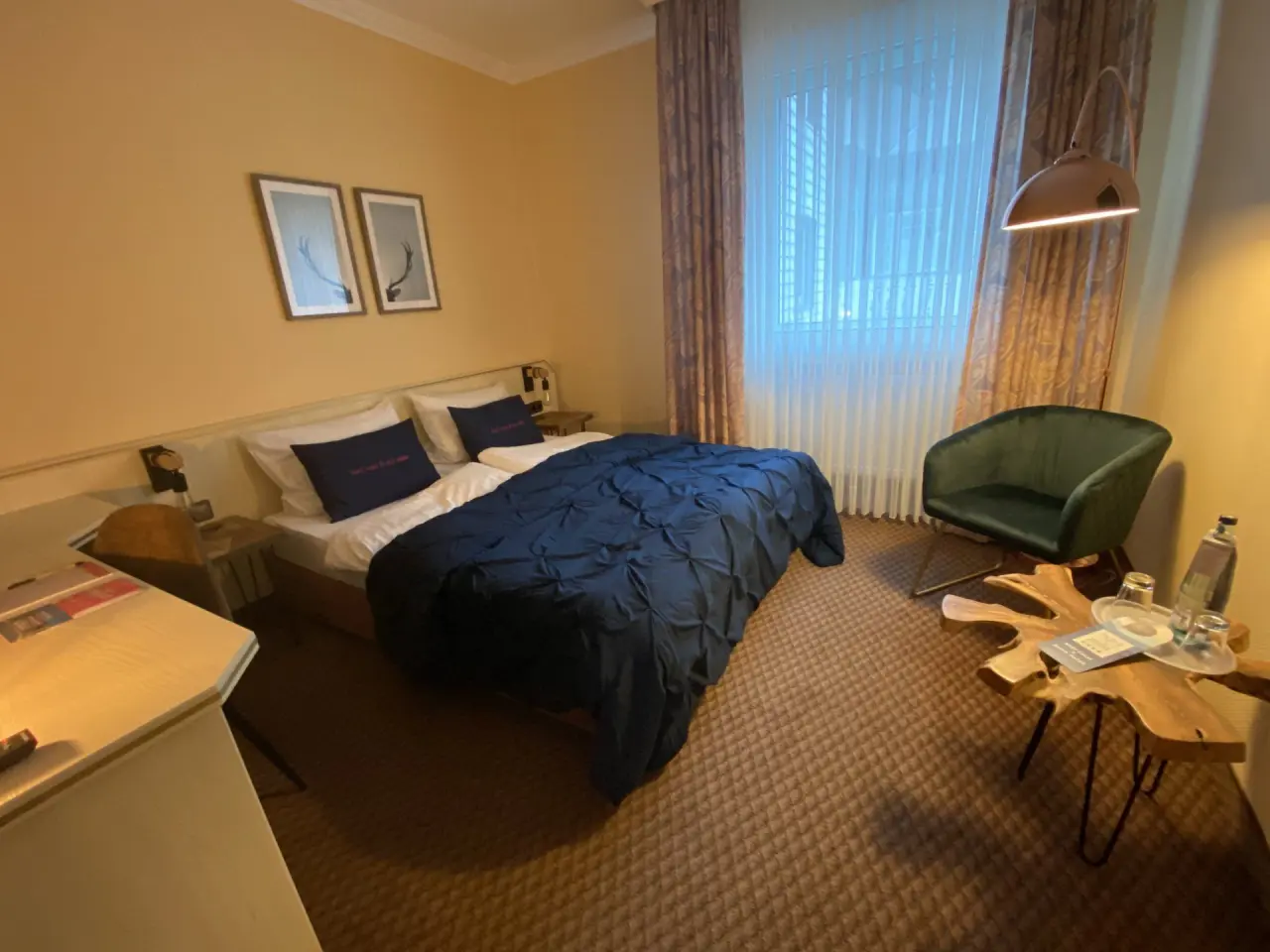 Gemütliches Doppelzimmer im Hotel Seela mit blauem Bett, grünem Sessel und rustikalem Holztisch.