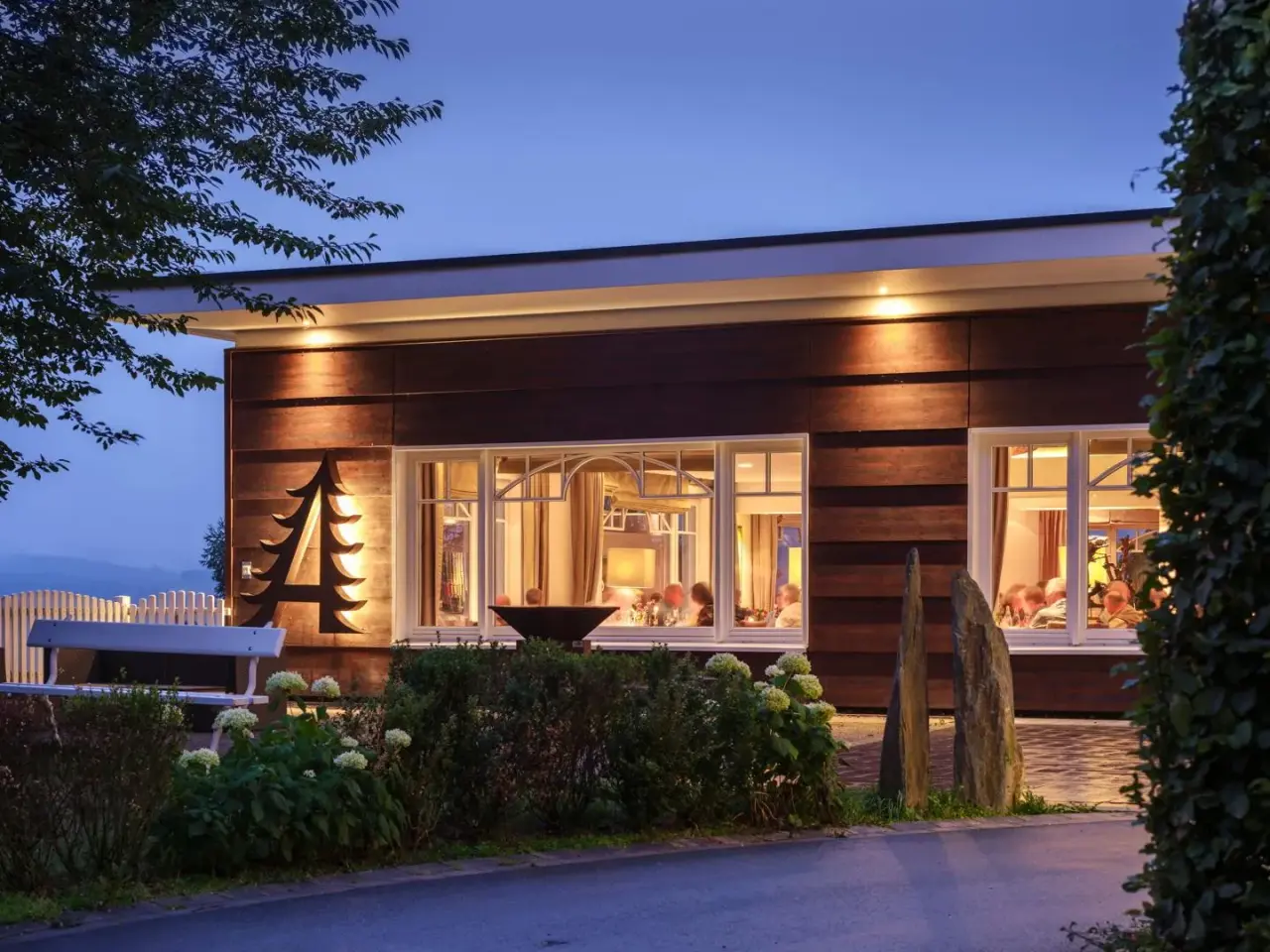 Abendliche Aussenansicht des Waldhaus Ohlenbach mit beleuchtetem Restaurant und markantem Baum-Logo.