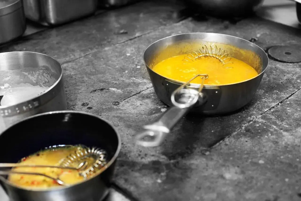 Zwei Töpfe mit gelber Sauce und Schneebesen in der Küche des Waldhaus Ohlenbach.