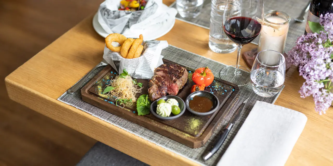 Exquisites Steak mit Beilagen, Rotwein und frischen Blumen auf Holztisch im Restaurant der Nationalpark Lodge Grossglockner.
