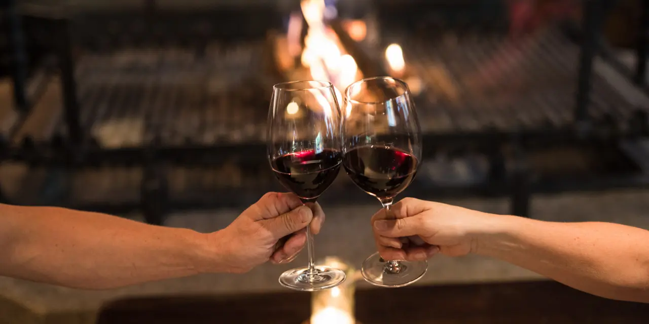 Zwei Personen stoßen mit Rotwein vor einem knisternden Kamin in der Nationalpark Lodge Grossglockner an.