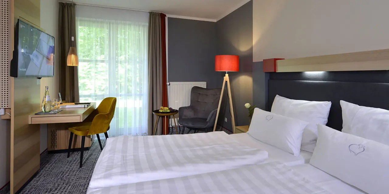 Modernes Doppelzimmer im Landhotel Schnuck mit bequemen Bett, Schreibtisch, Sessel und Blick ins Grüne.