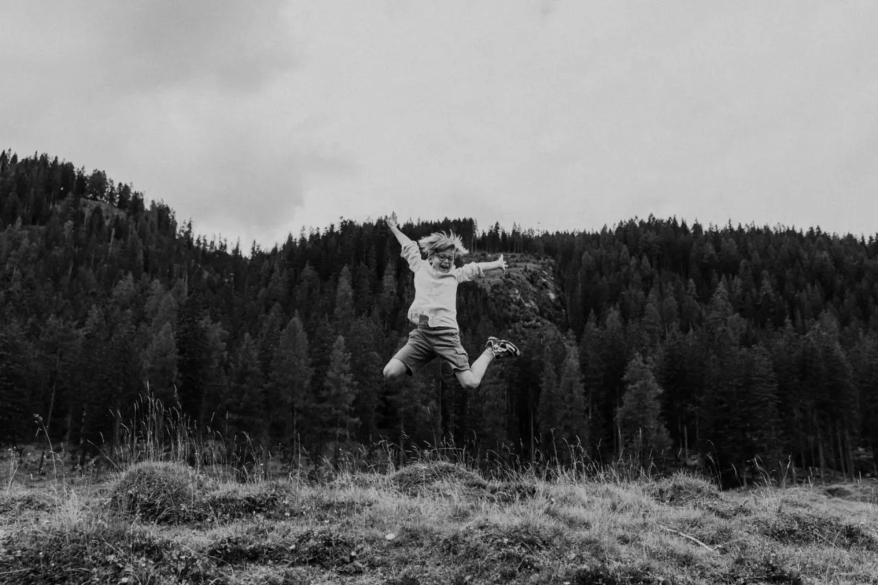 Fröhlich springendes Kind in einer Bergwiese vor einem Wald, symbolisiert Outdoor-Aktivitäten nahe Hotel Steiner.