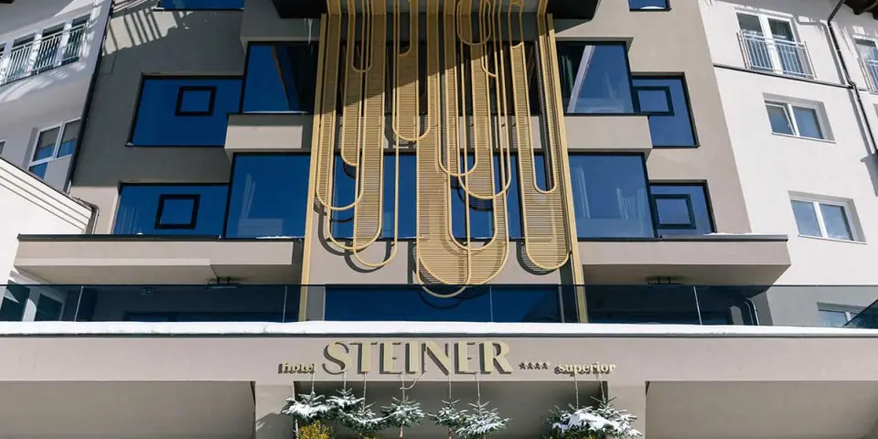 Moderne Fassade des Hotel Steiner **** superior im Winter mit markanter goldener Dekoration und Schnee.