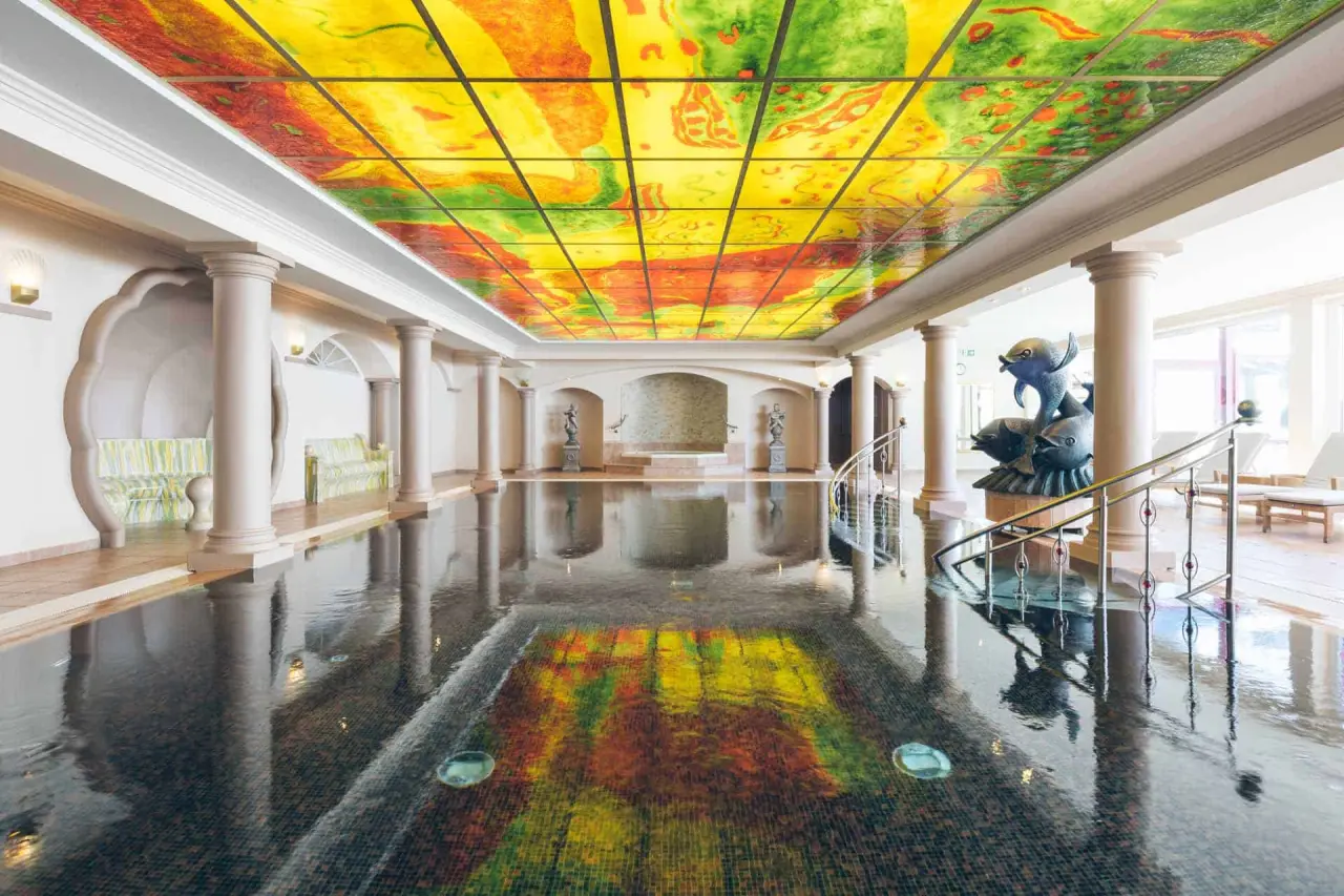 Innenpool mit farbenfroher Decke und Whirlpool im Hotel Steiner. Einladende Wellness-Oase für Entspannung.