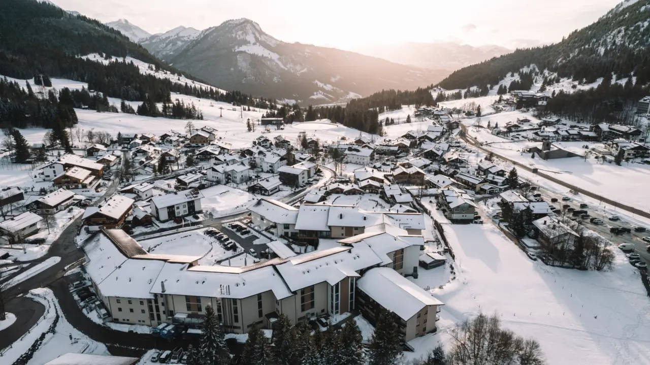 Luftaufnahme des Parkhotel Jordanbad in einem verschneiten Bergdorf mit Alpenpanorama und warmem Abendlicht.