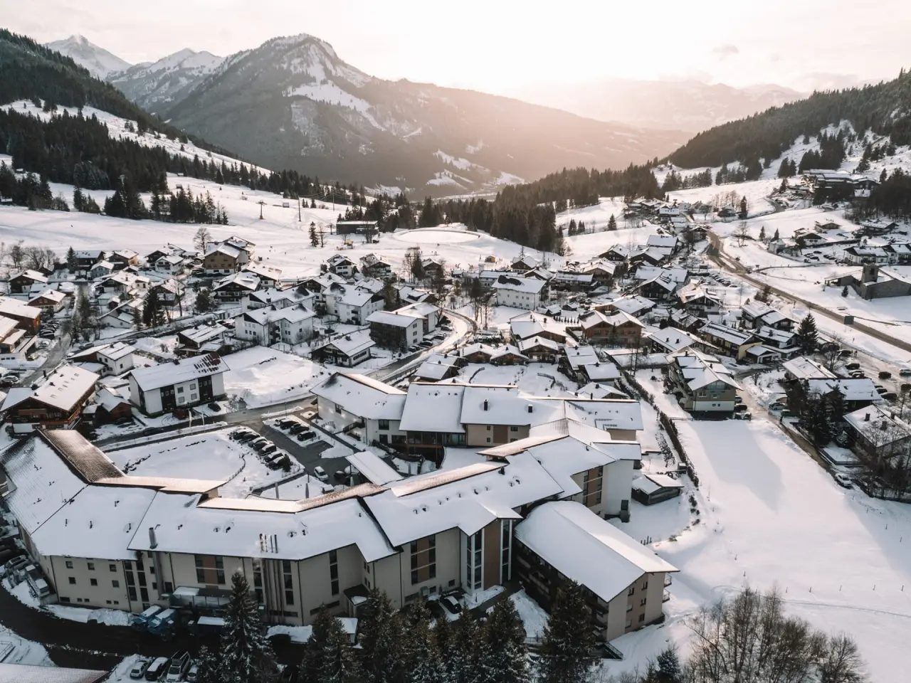 Luftaufnahme des Parkhotel Jordanbad im Winter, eingebettet in ein verschneites Alpendorf mit majestätischem Bergpanorama.
