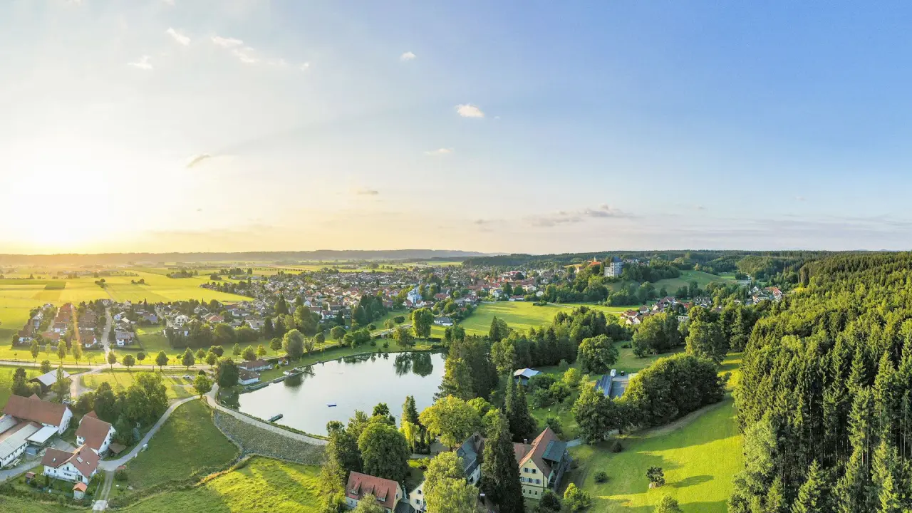 Idyllischer Panoramablick auf das Bad Clevers Gesundheitsresort & Spa mit See, grünen Wiesen und Wäldern im Abendlicht.