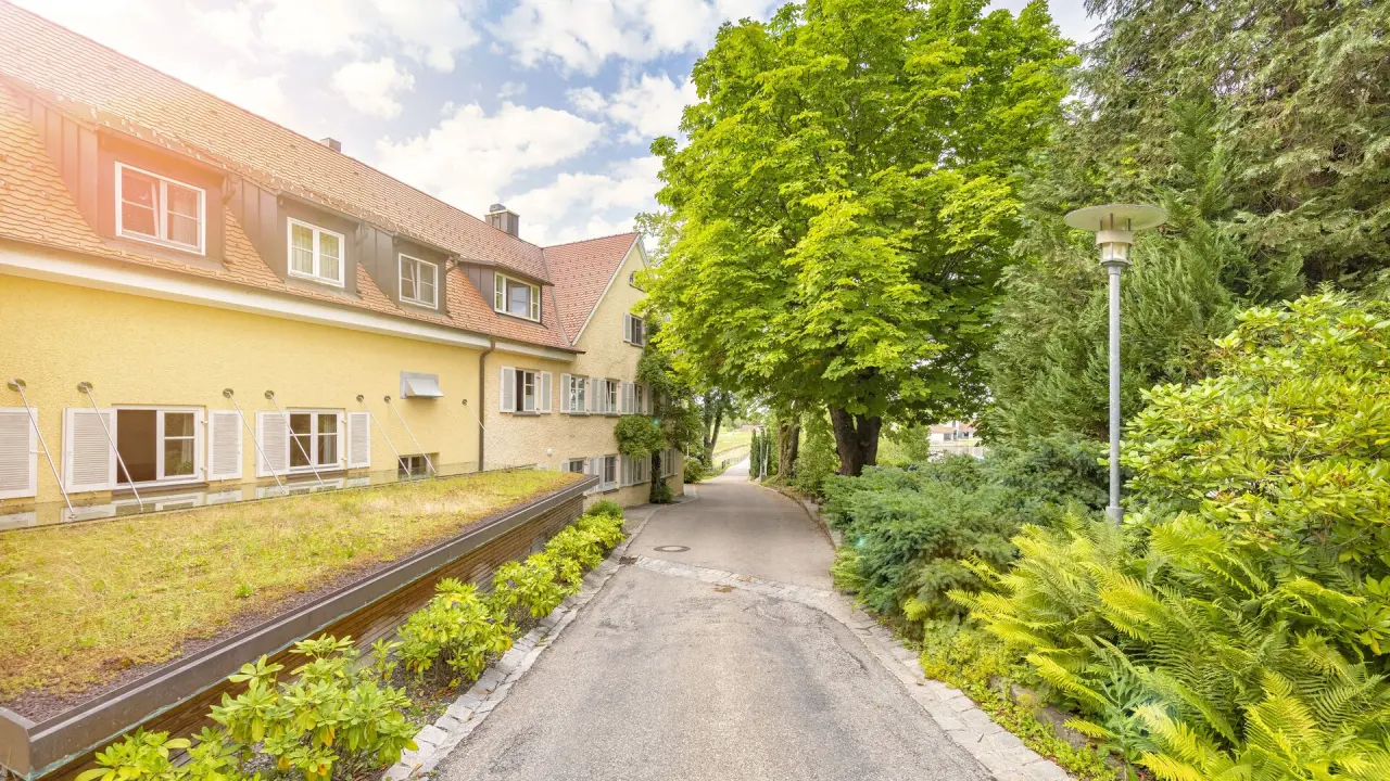 Aussenansicht des Bad Clevers Gesundheitsresort & Spa mit gelbem Gebäude, begrüntem Dach und idyllischem Weg im Grünen.