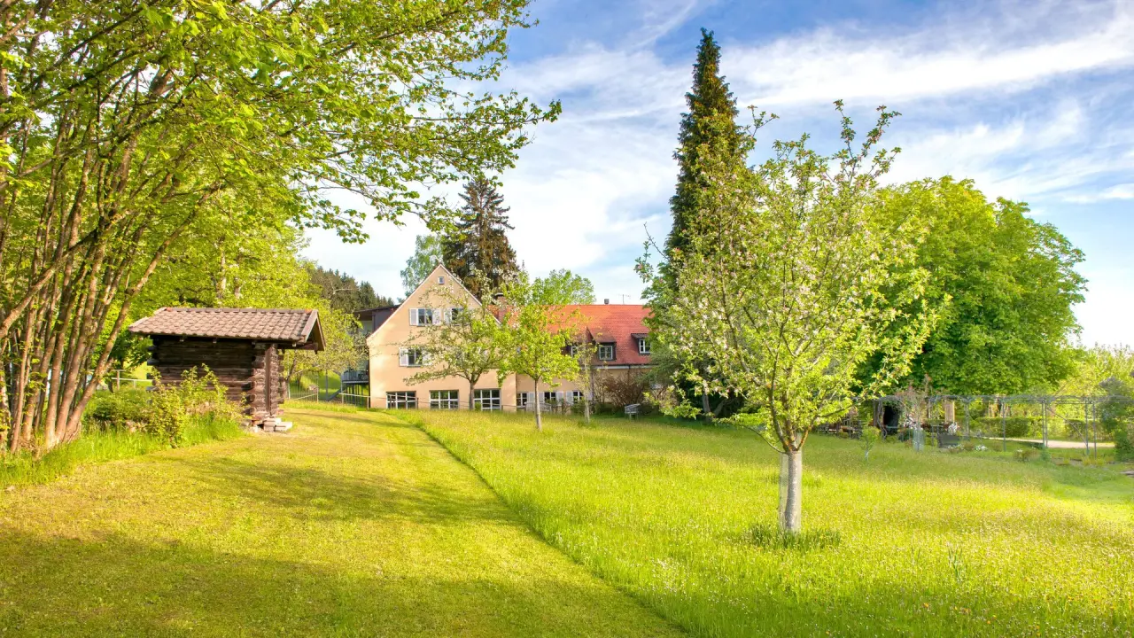 Frühlingshafte Gartenanlage mit dem historischen Gebäude des Bad Clevers Gesundheitsresort & Spa unter blauem Himmel.