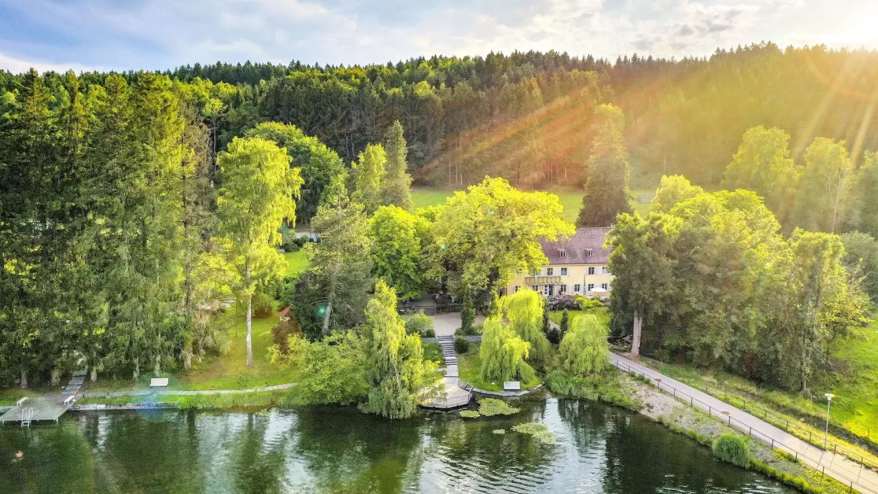 Malerisches Bad Clevers Gesundheitsresort & Spa am See, eingebettet in grüne Wälder mit strahlender Abendsonne.