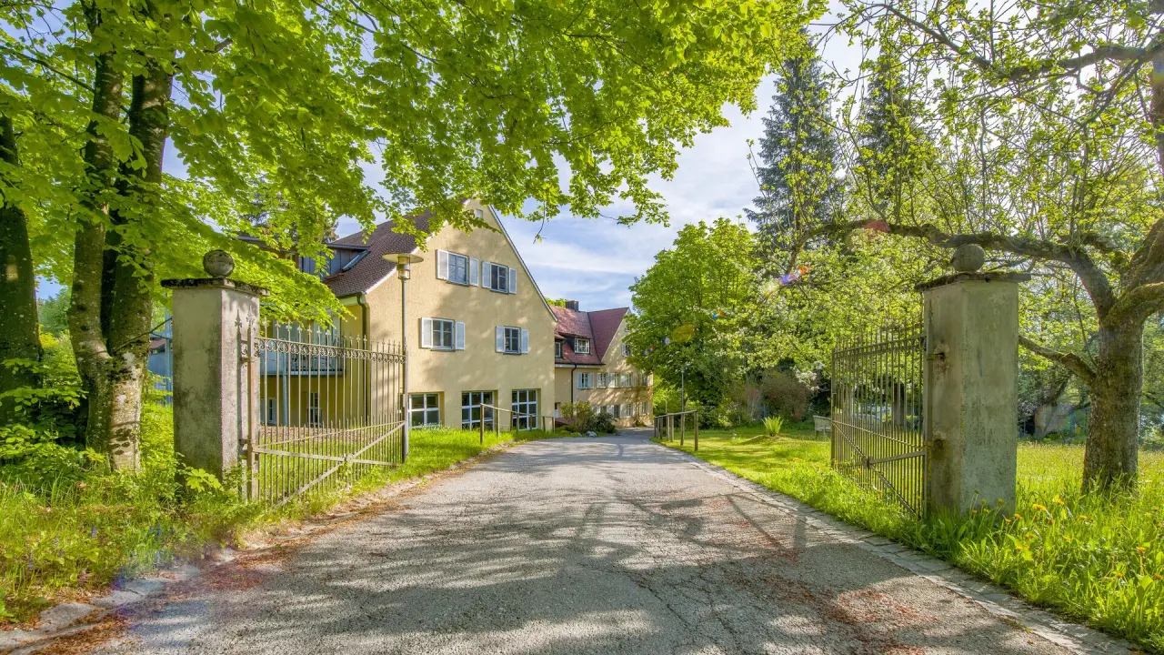 Eingang zum Bad Clevers Gesundheitsresort & Spa mit von Bäumen gesäumter Auffahrt und historischem Tor im Frühling.