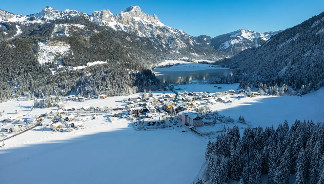 Panoramablick auf das Hotel Tyrol am Haldensee im Winter, umgeben von verschneiten Bergen und einem teilweise zugefrorenen See.