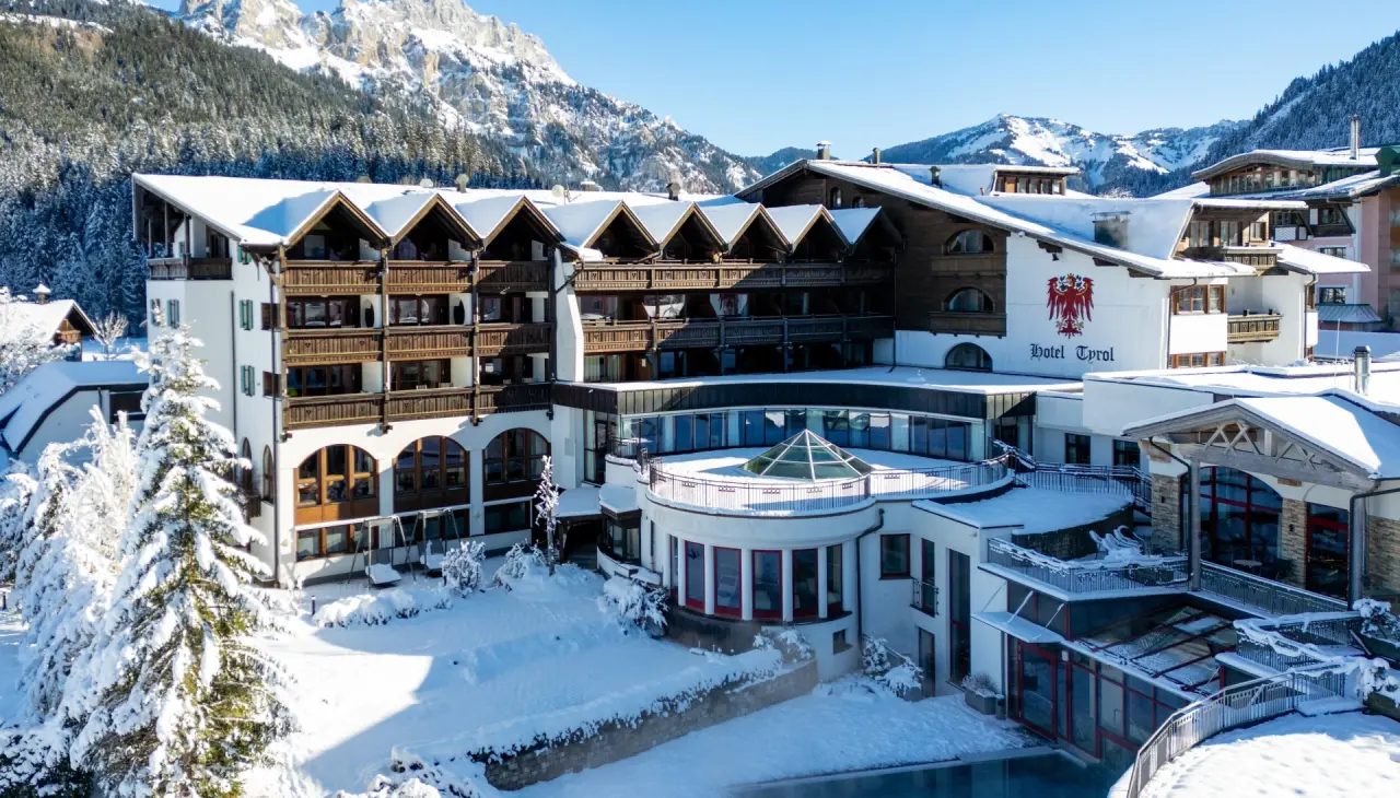 Hotel Tyrol am Haldensee im Winter, umgeben von verschneiten Bergen und Tannen, mit traditioneller alpiner Architektur.