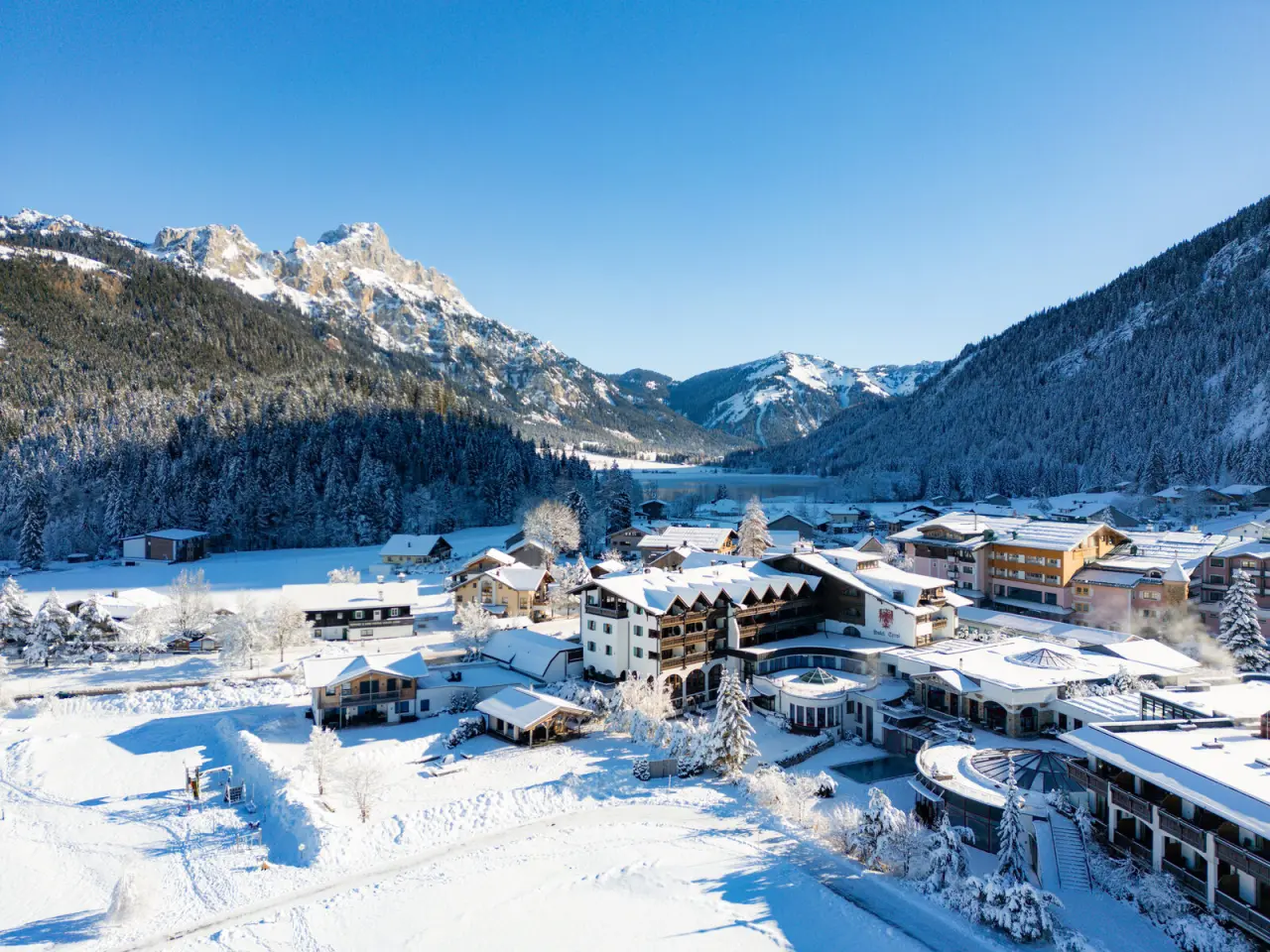 Luftaufnahme des Hotel Tyrol am Haldensee im Winter, umgeben von schneebedeckten Bergen und dem zugefrorenen See.