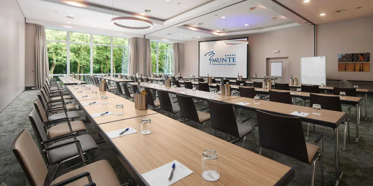 Modern eingerichteter Konferenzraum im Hotel Munte am Stadtwald mit Blick ins Grüne und Projektionsfläche.