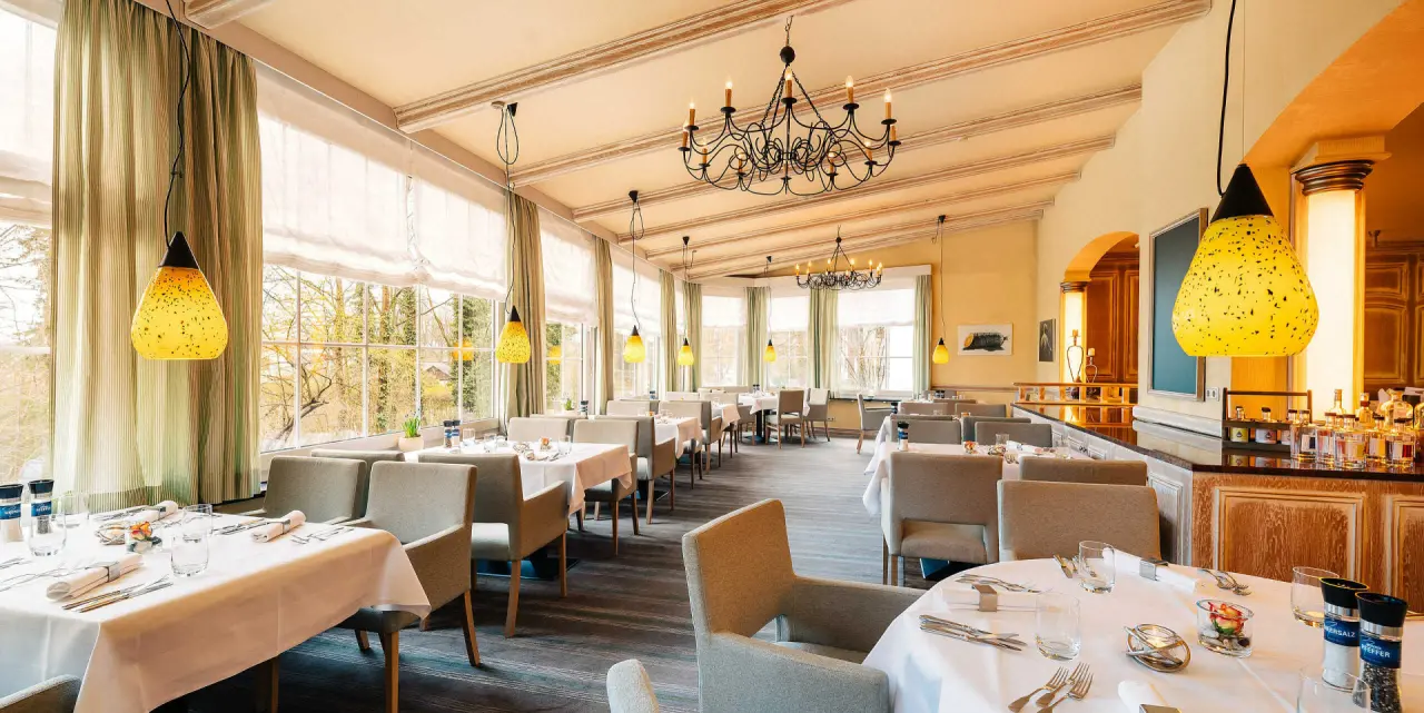 Elegantes Restaurant im Hotel Munte am Stadtwald mit großen Fenstern, stilvollen Tischen und Blick auf die Natur.
