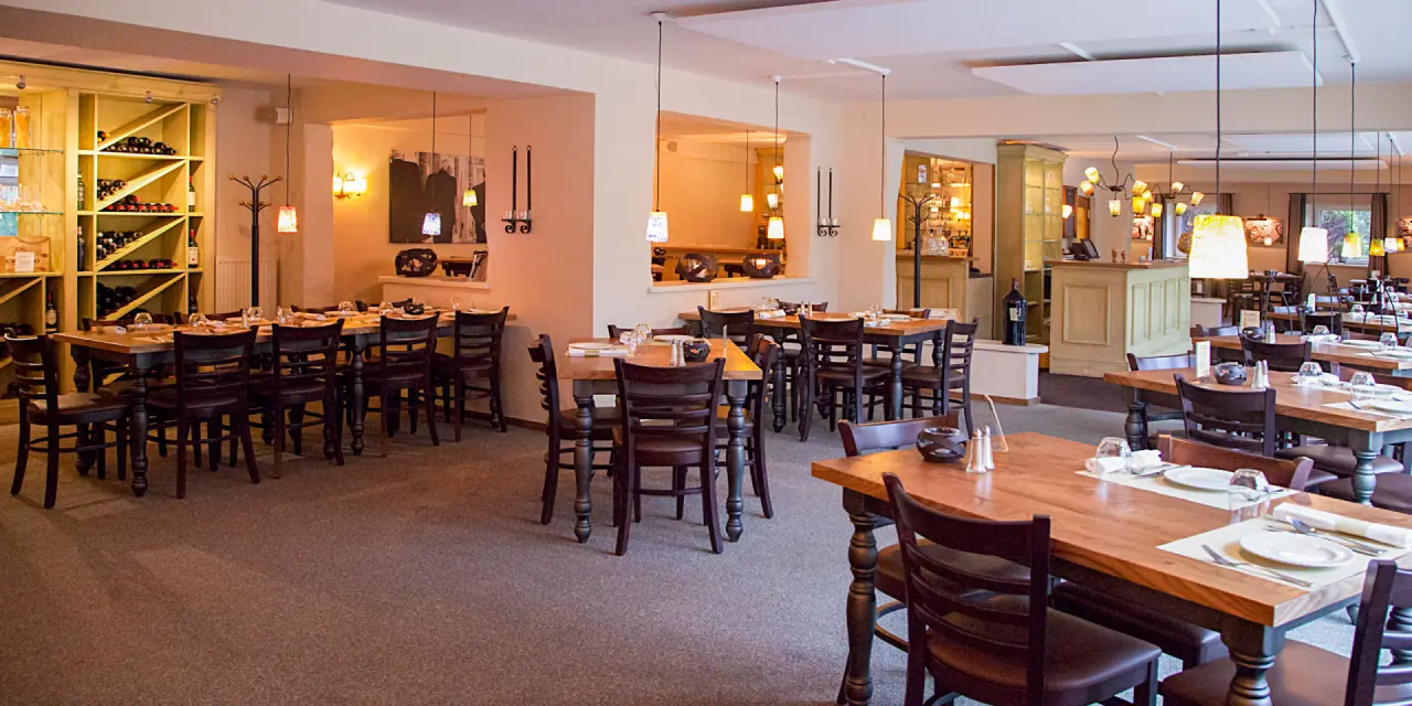 Geräumiges Restaurant im Hotel Munte am Stadtwald mit Holztischen, Stühlen und Weinregal.